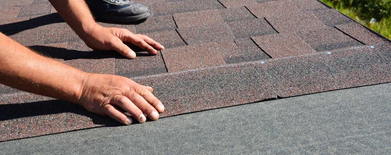 Person installing asphalt shingles on a roof.