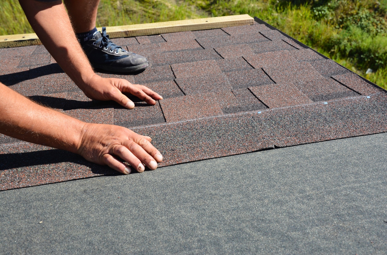 Person installing asphalt shingles on a roof.