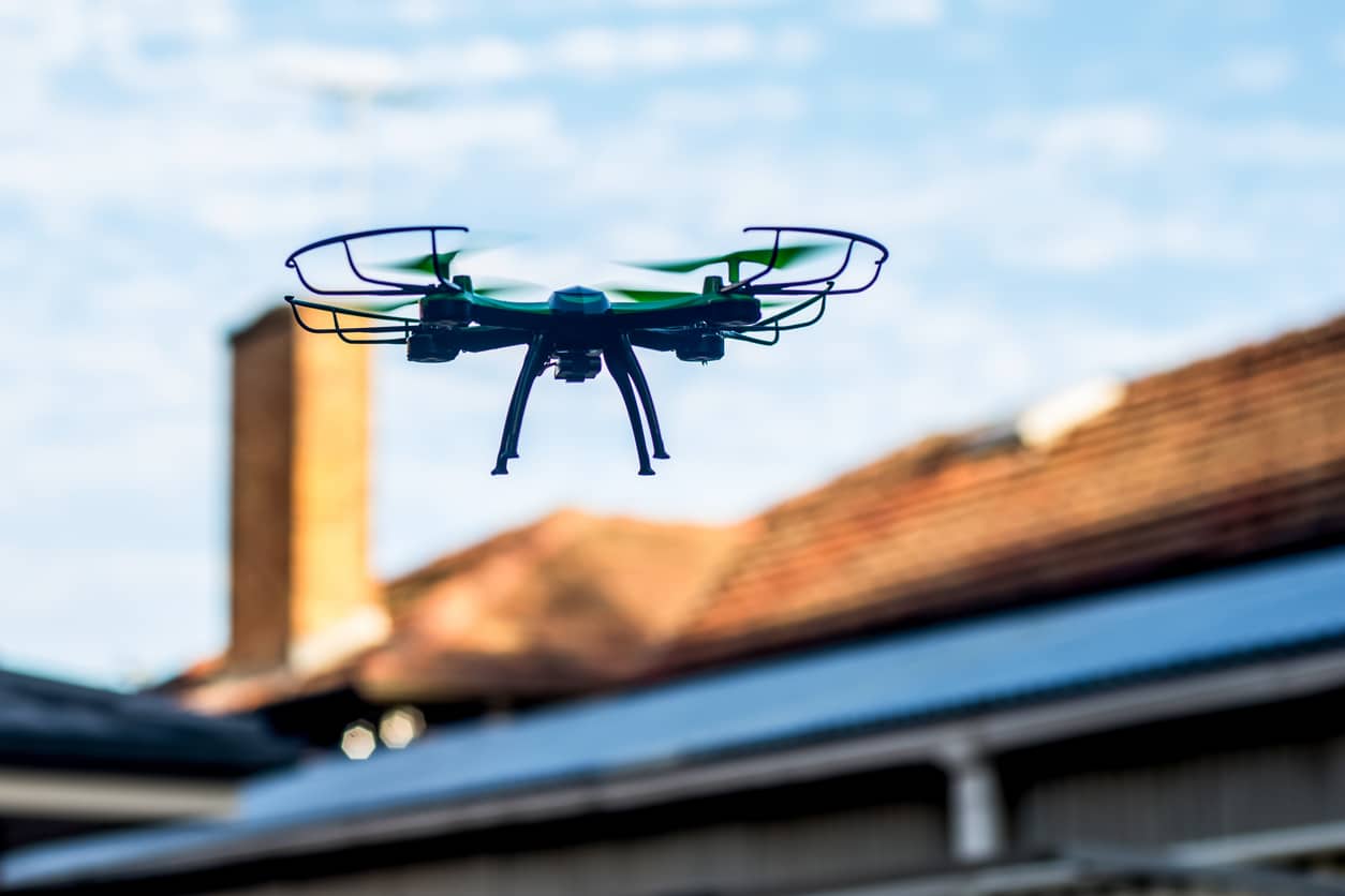 Drone flying over rooftops on a clear day, capturing aerial views.