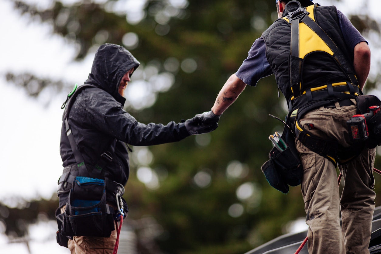 Two workers in safety gear, shaking hands outdoors, symbolizing teamwork and cooperation.