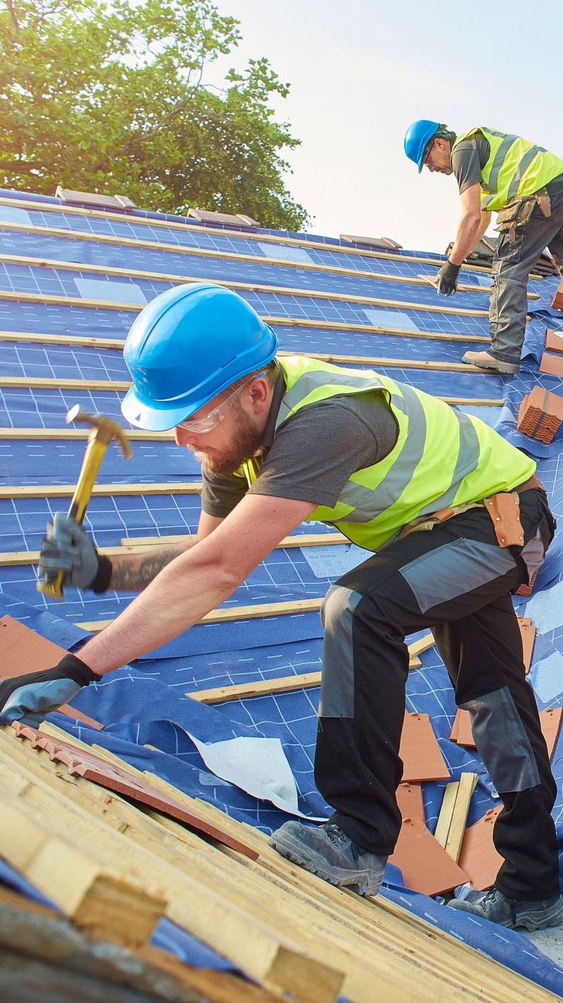 Construction workers installing roofing with safety gear on a sunny day.